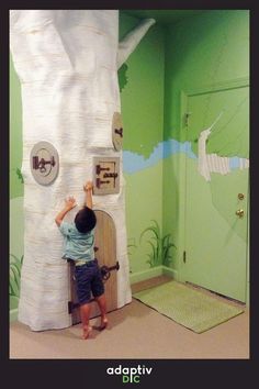 a young boy climbing up the side of a fake tree in a room with green walls