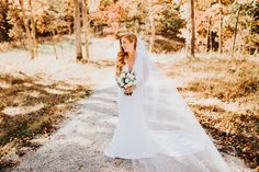 a woman in a wedding dress standing on a dirt road with trees and leaves around her