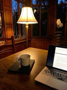 a laptop computer sitting on top of a wooden table next to a cup of coffee