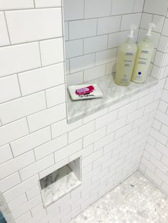 a white tiled bathroom with two bottles of hand soap on the shelf and a pink toothbrush next to it