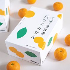 two boxes with oranges in front of them on a white surface, surrounded by small tangerines