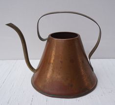 an old metal tea pot with a curved handle on a white wooden tableclothed surface