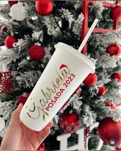 someone holding up a starbucks cup in front of a christmas tree with red and white ornaments