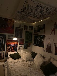 an unmade bed in a room with posters on the wall and lights above it