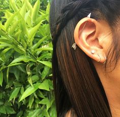 a close up of a person's ear with an earring in front of some bushes