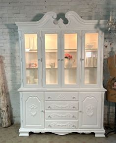 a white china cabinet with glass doors and drawers in a room next to a guitar