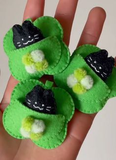 a hand is holding three small green shoes with black and white cat faces on them