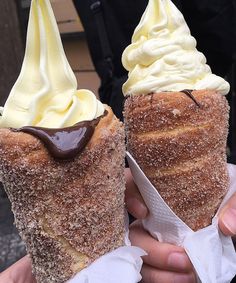 two dessert cones with chocolate sauce and whipped cream on top are being held by someone's hand