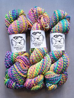 three skeins of multicolored yarn on a gray surface with white labels