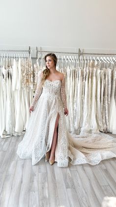 a woman standing in front of a rack of wedding dresses