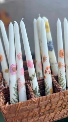 there are many candles in the basket on the table and one is white with floral designs