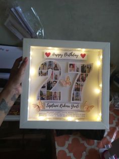 someone is holding up a birthday card with photos and lights on it in front of a table