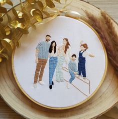 a cross - stitch family portrait on a wooden plate with gold ribbon and golden leaves