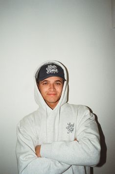 a young man wearing a white hoodie and black hat with his arms crossed in front of him