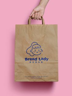 a person holding a brown paper bag with the words bread lady on it, against a pink background