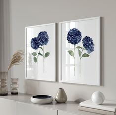 two blue flowers are displayed on the wall above a white dresser with vases and other items