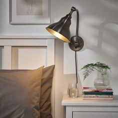 a lamp on a wall next to a bed with pillows and a vase in the corner