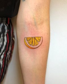 a small orange slice tattoo on the left leg by a person's legs and arm