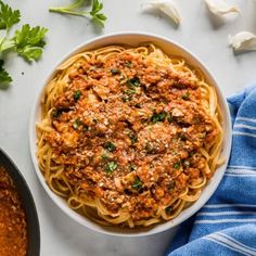 a bowl of spaghetti with meat sauce and parsley on the side next to it