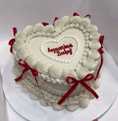 a heart shaped cake with red ribbon around it on a white platter in a box