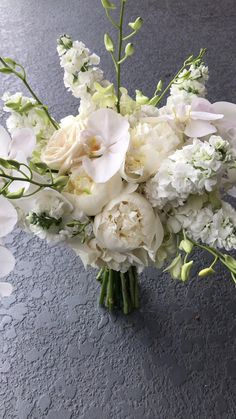 a bouquet of white flowers and greenery in a vase on the floor with dark background