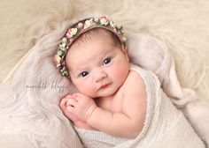 a baby wearing a flower headband laying on top of a blanket