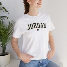 P R O D U C T O V E R V I E W Jordan University Style Letters with Flag, Unisex T-Shirt Bella+Canvas 3001 P R O D U C T D E T A I L S * 100% Airlume combed and ringspun cotton (fiber content may vary for different colors) * Light fabric  * Retail fit * Tear away label * Runs true to size R E T U R N P O L I C Y * All of our shirts are custom printed just for you so we do not accept returns or exchanges due to size. * If there are any issues with the shirt, please message us and we will replace i White Embroidered T-shirt For College, Sporty Embroidered Graphics T-shirt, White Embroidered Graphics T-shirt For College, Sporty Cotton T-shirt With Embroidered Graphics, Short Sleeve Tops With Embroidered Graphics For College, Short Sleeve T-shirt With Embroidered Graphics For College, University Style, Cotton Fiber, Shirt Price