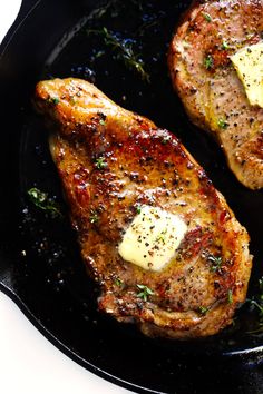 two pieces of meat in a skillet with butter and herbs on top, sitting next to each other