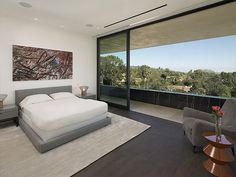 a bedroom with a large white bed sitting next to a glass wall and a painting on the wall