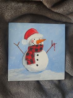 a painting of a snowman wearing a santa hat and scarf on a gray blanket