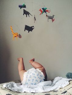 a baby laying on top of a bed next to a wall with animals hanging from it