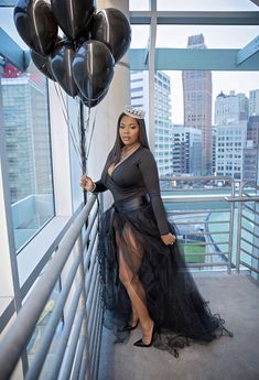 a woman in a black dress is holding balloons and posing for the camera with her hands on her hips