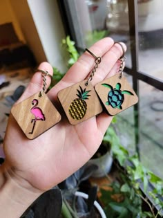 two wooden keychains with different designs on them in front of a glass window