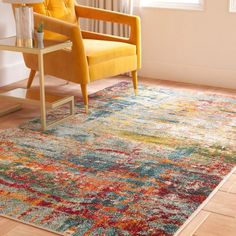 a yellow chair sitting on top of a wooden floor next to a rug covered in multicolored paint