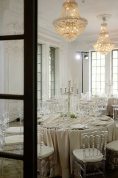 a room filled with tables and chairs covered in white tablecloths next to tall windows