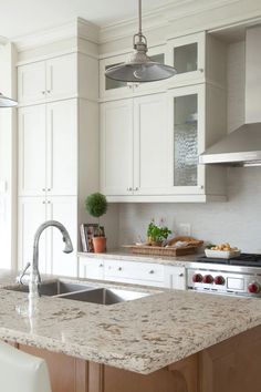 a kitchen with white cabinets and marble counter tops, an island sink and stainless steel appliances