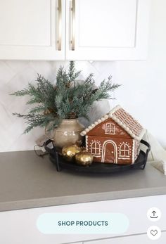 a gingerbread house on a tray with christmas decorations in front of white cupboards