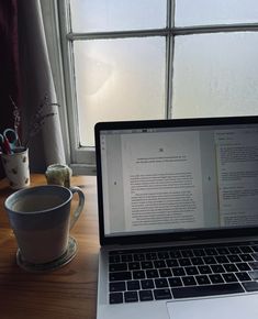 an open laptop computer sitting on top of a wooden desk next to a coffee cup