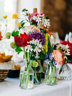 several vases filled with different types of flowers on a white tablecloth covered table