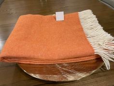 an orange and white blanket sitting on top of a wooden table next to a bowl