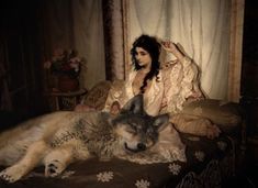 a woman sitting on top of a bed next to a wolf