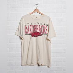 Our Best Selling University Of Arkansas Razorbacks Design Printed On An Ivory Comfort Colors Classic Fit T-Shirt That You’ll Wear Over And Over. Officially Licensed With The Ncaa! Comfort Colors Is A T-Shirt Brand With A Worn-In Softness, A Faded Natural Color, And A Relaxed Fit That’s Familiar Like An Old Friend. Comfort Colors Apparel Has A Relaxed Fit Compared To Other Brands. That Means Slightly Oversized, Especially Compared To Fashion Fit/Slim Fit T-Shirts. 6.1 Oz., 100% Ring Spun Cotton N Arkansas Shirt, Cute College Shirts Design, High School Tshirt Design, Company Shirt Design, College Graphic Tee, Vintage School Shirts, College Shirts Design, School Tshirt Designs Spirit Wear, College Tshirt Designs