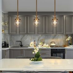 a kitchen with grey cabinets and white counter tops, lights hanging over the island table