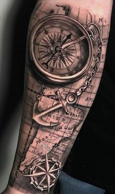 a man's arm with a compass, compass and other items tattooed on it