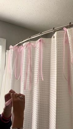 a person standing in front of a shower curtain with pink ribbon on it's edge