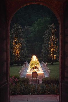 a long table with chairs and lights on it in the middle of a garden at night