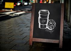 a chalkboard sign with a coffee cup drawn on it in front of a street