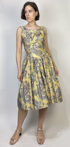 -->DESCRIPTION<-- Vintage 50s GORGEOUS golden yellow dress with matching bolero! So classic, slightly drop waist cut with full crinoline skirt and bow and rhinestone detail. Love the oversized paisley print and dreamy, almost southwest colour scheme. The bolero can be worn separately as a low cut crop top! No tags, dress is fully lined, does up with a steel zipper. -->CONDITION<-- Pristine condition! -->FABRIC<-- No tag to indicate, has a slight sheen, feels like a brushed cott Yellow Cocktail Dress With Fitted Bodice, Yellow Elegant Dress With Pleated Bodice, Gold Fitted Dress With Pleated Bodice, Yellow Fitted Dress With Pleated Bodice, Fitted Yellow Dress With Pleated Bodice, Formal Sleeveless Dress With Gathered Skirt, Elegant Yellow Fit And Flare Dress, 1950s Style Yellow Dress For Garden Party, Yellow 1950s Style Dress For Garden Party