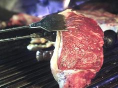 steaks being cooked on the grill with tongs in their mouth and meat cooking over it