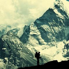 a man with a backpack standing on top of a mountain looking at the snow covered mountains